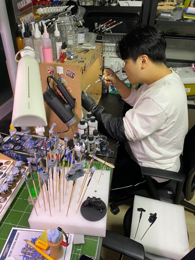 Model maker airbrushing miniature parts at a detailed workbench
